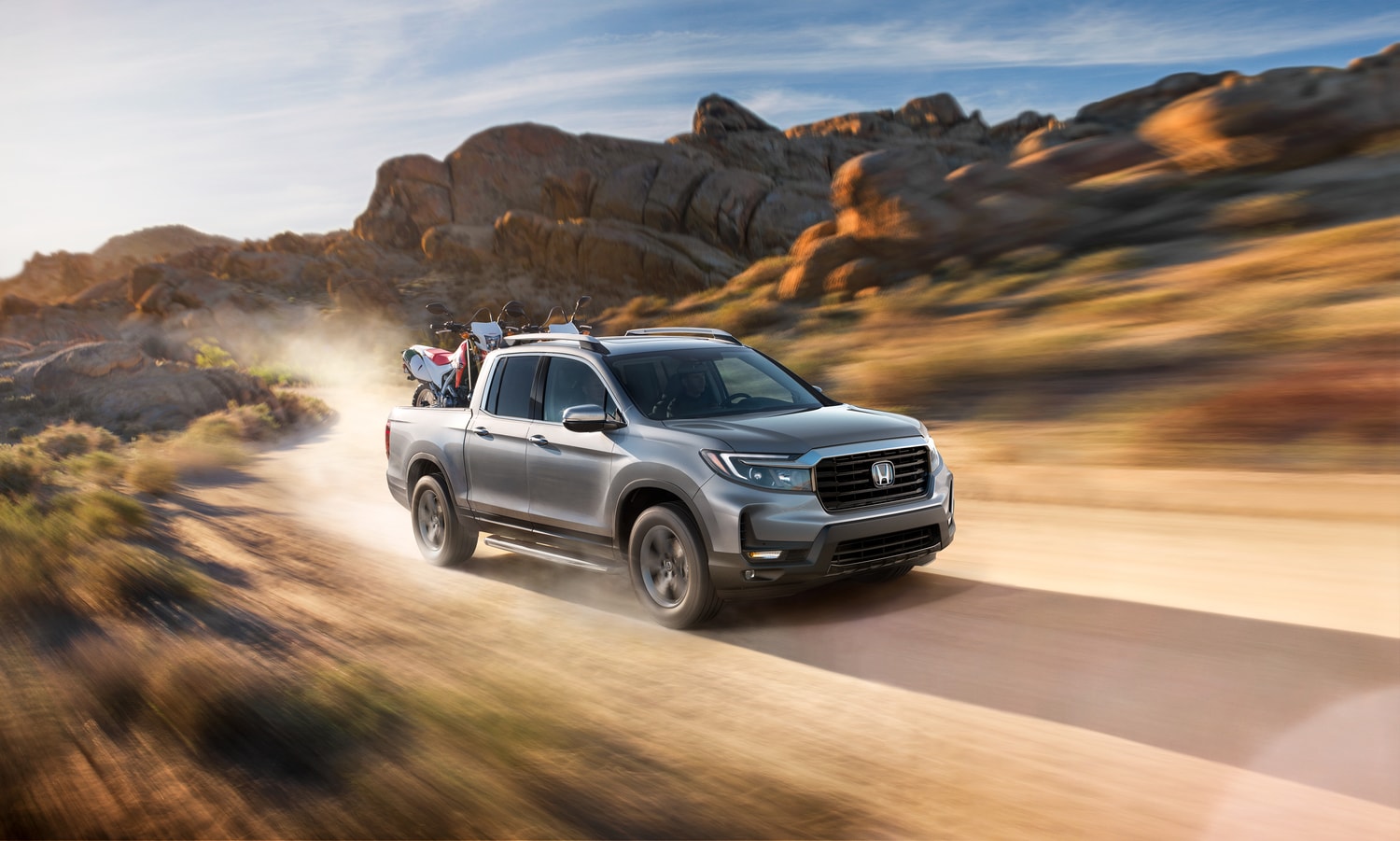 2024-Honda-Ridgeline-RTL-Truck-L03.png silver Honda Ridgeline truck driving on a dusty desert road
