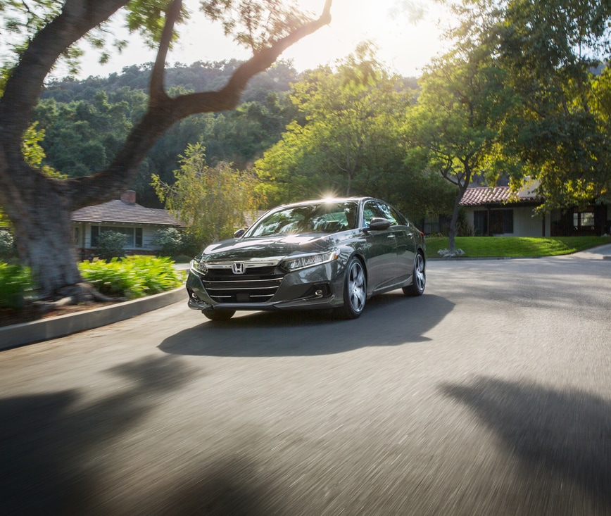 2022-Honda-AccordHybrid-Touring-Sedan-L04.png sliver Honda Accord hybrid sedan driving through a suburban neighborhood