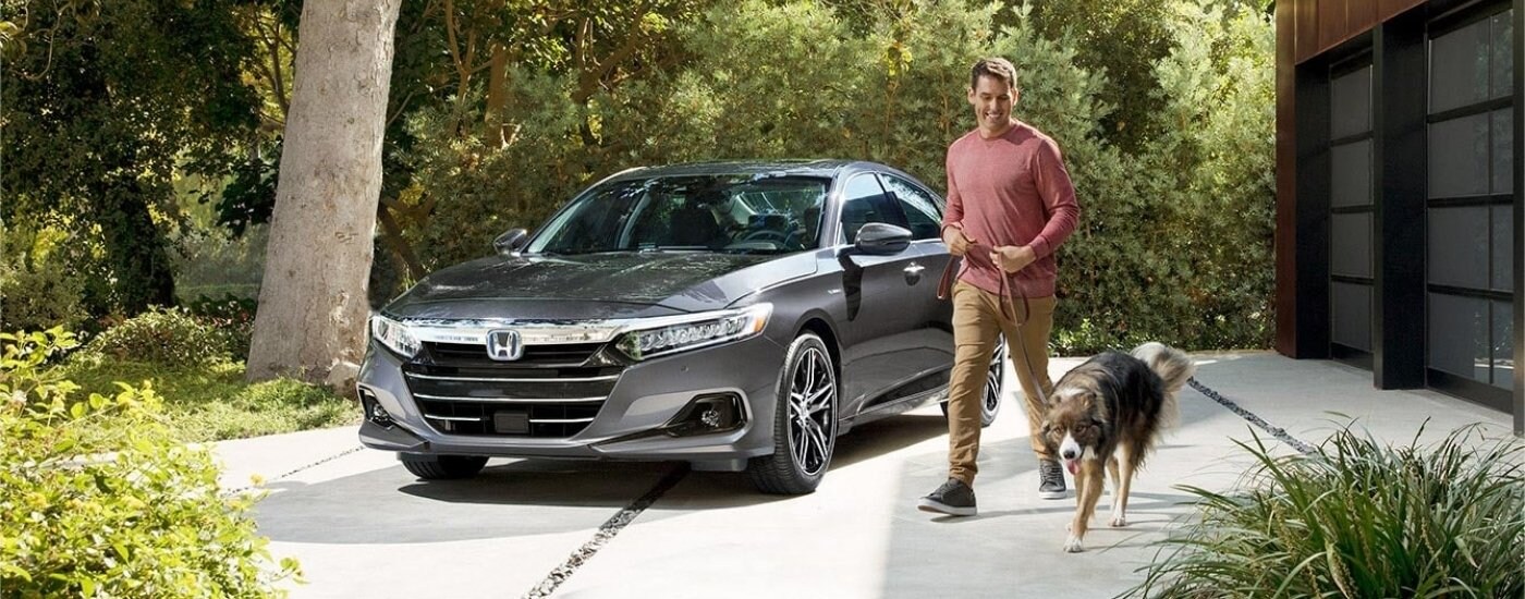 A gray 2021 Honda Accord Hybrid parked by a man and dog.