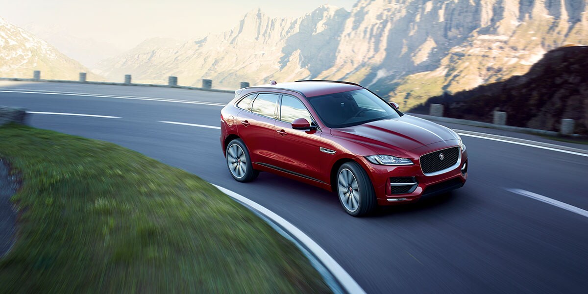 RED JAGUAR F-PACE DRIVING DOWN CURVED ROAD IN MOUNTAINS.