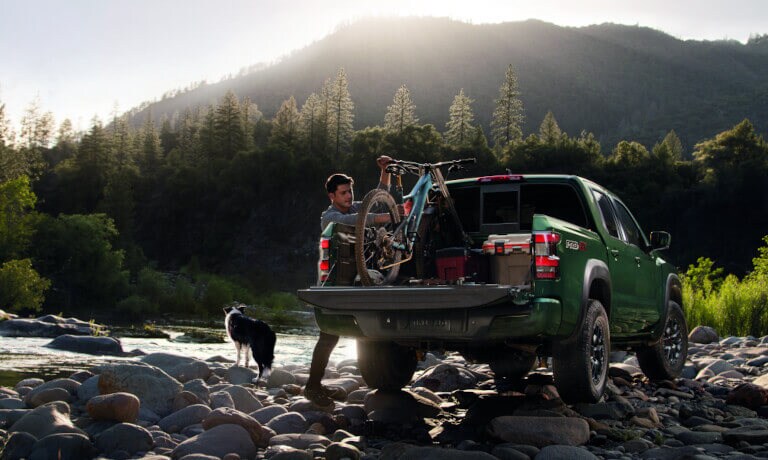 Person loading bike into the bed of a 2022 Nissan Frontier while a good dog stands watch