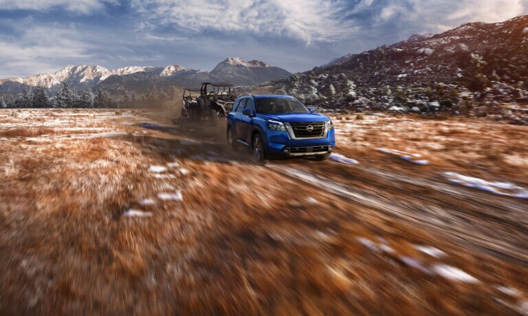 2022 Nissan Pathfinder towing a tractor through a field