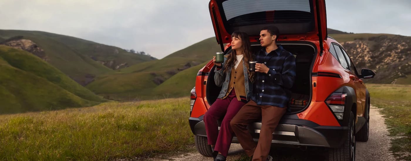 Two people sitting in the back of a red 2026 Hyundai Kona parked off-road.