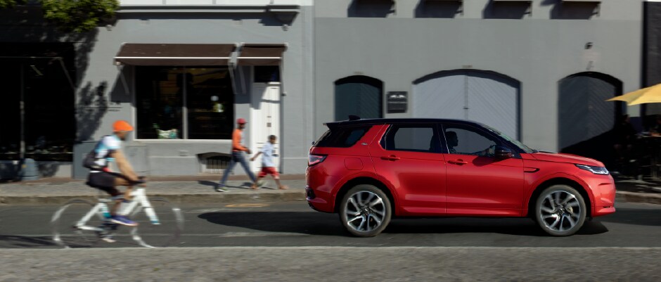 RED LAND ROVER DISCOVERY SPORT DRIVING DOWN STREET IN CITY