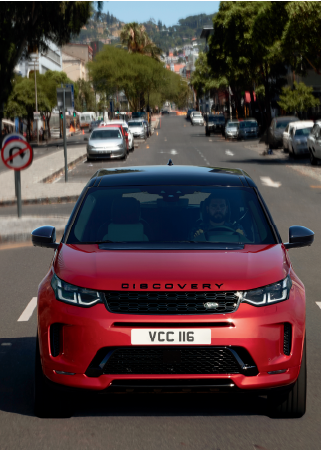 RED LAND ROVER DISCOVERY SPORT DRIVING DOWN STREET IN CITY