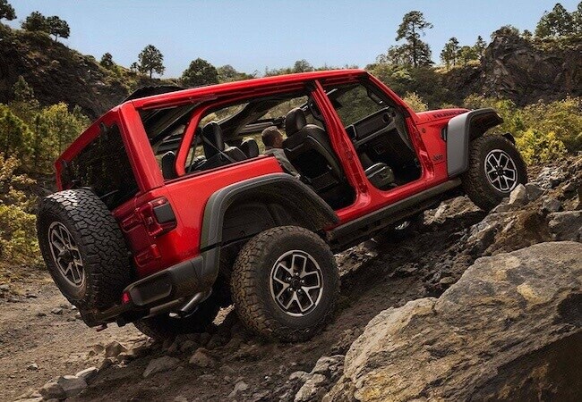 Red 2026 Jeep Wrangler Rubicon climbing over large rocks on a technical off-road trail