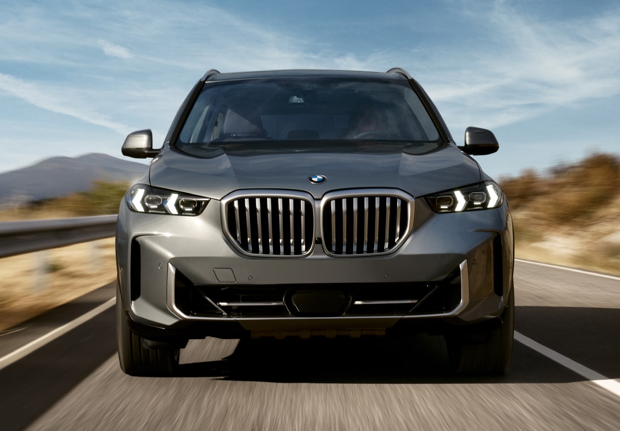 A front view of a gray BMW X5 driving down the highway. A front view of a gray BMW X5 driving down the highway.