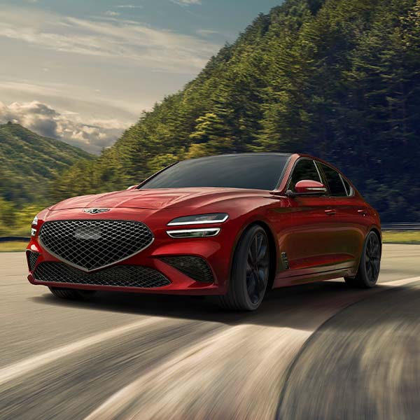 Model Features of the 2022 Genesis G70 at Genesis of York | Red 2022 Genesis G70 Driving on Roads Past Lush Green Mountains at Sunset