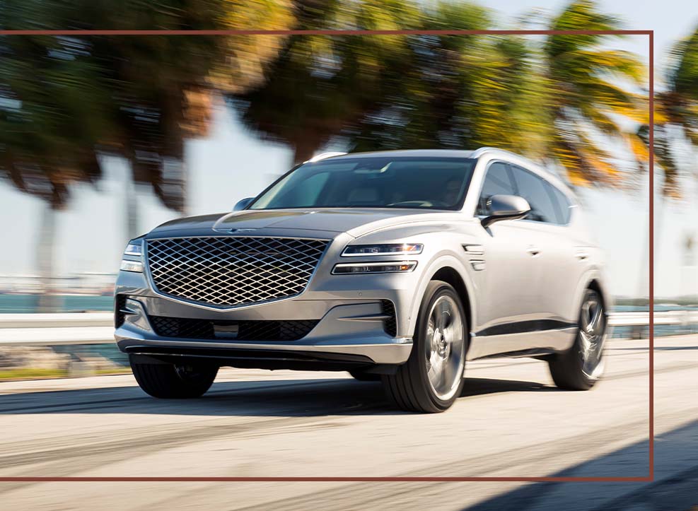 Compare the 2021 Genesis GV80 vs. the 2021 Audi Q7 at Genesis of York | Silver 2021 Genesis Driving Fast Down Coastal Highway