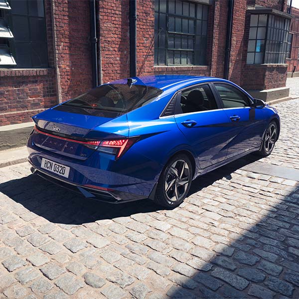 Model Features of the 2022 Hyundai Elantra at Jack Giambalvo Hyundai | Rearview of Blue 2022 Hyundai Elantra Driving Through Alleyway in Between Buildings in City