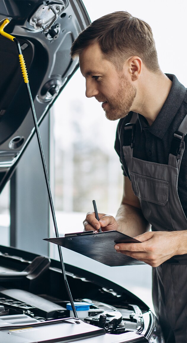Vehicle Warranty Information at Jack Giambalvo Hyundai in York, PA | Mechanic in grey uniform is inspecting underneath the car hood with clipboard