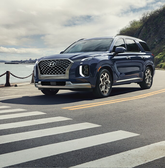 Best MPG At Jack Giambalvo Hyundai in York, PA | Dark blue 2023 Hyundai Palisade driving down a road about to pass a crosswalk