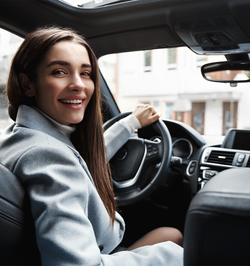 Extend the Life of Your Vehicle at Jack Giambalvo Hyundai in York, PA | Woman in grey jacket is looking behind her driver seat while smiling