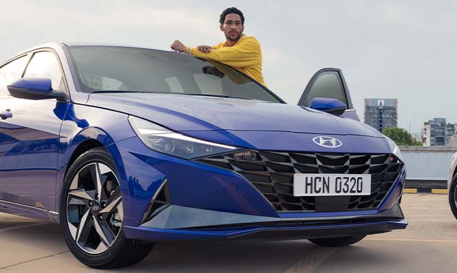 Model Features of the 2022 Hyundai Elantra at Jack Giambalvo Hyundai | Man in Bright Yellow Sweater Leaning on Blue 2022 Hyundai Elantra