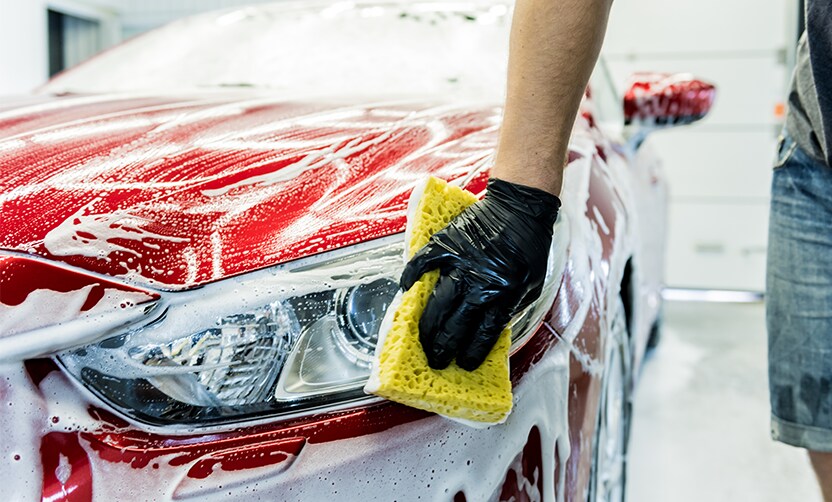 Extend the Life of Your Vehicle at Jack Giambalvo Hyundai in York, PA | Person with black gloves is using a yellow sponge to clean their red car with soap and water