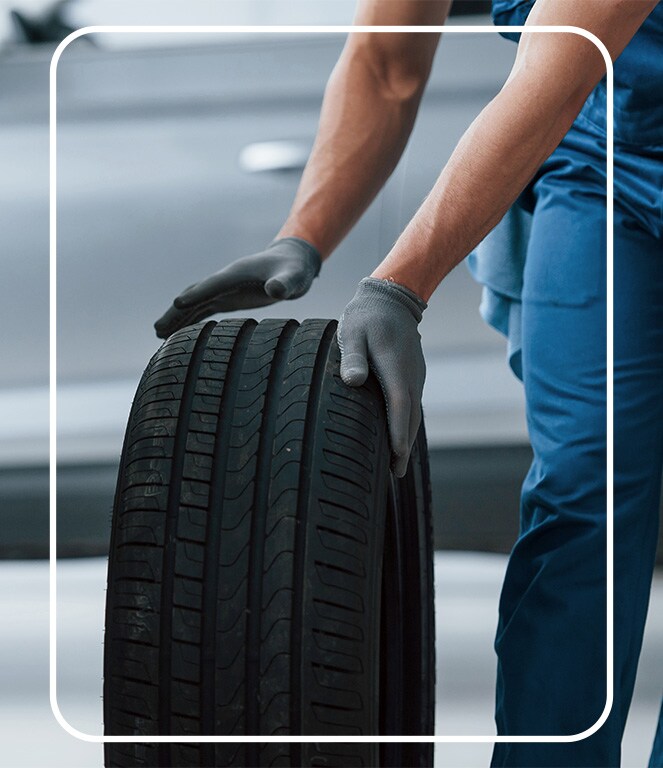 The Cold Facts of Winter Tires | Jack Giambalvo Hyundai in York, PA | Mechanic rolling old car tire on the floor while wearing grey color gloves