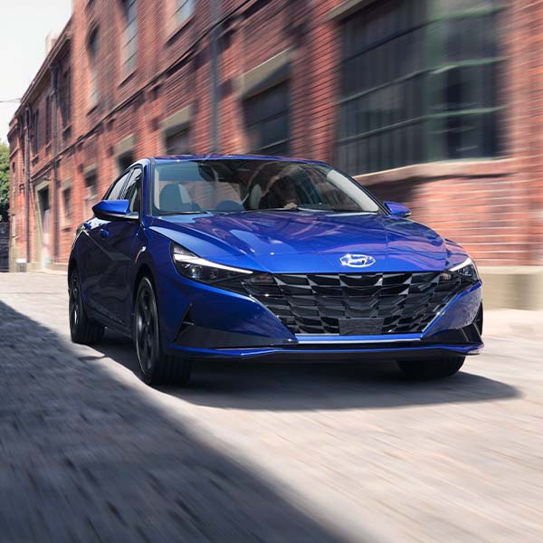 Model Features of the 2022 Hyundai Elantra at Jack Giambalvo Hyundai | Blue 2022 Hyundai Elantra Driving Through Alleyway in Between Buildings in City