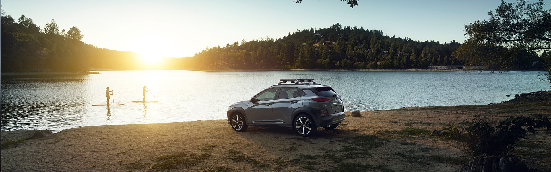 Jack Giambalvo Hyundai is a Hyundai Dealership in York near Dover, PA | A 2019 Hyundai Kona parked lakeside by 2 paddleboarders at sunset