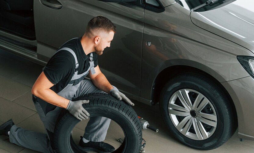 Extend the Life of Your Vehicle at Jack Giambalvo Hyundai in York, PA | Mechanic in black shirt and grey overalls in installing new car tire to a silver car