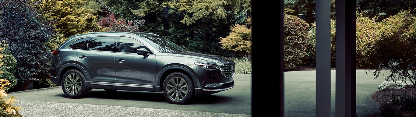 Best MPG At Jack Giambalvo Mazda in York, PA | Grey 2023 Mazda CX-9 parked in front of driveway with trees behind it