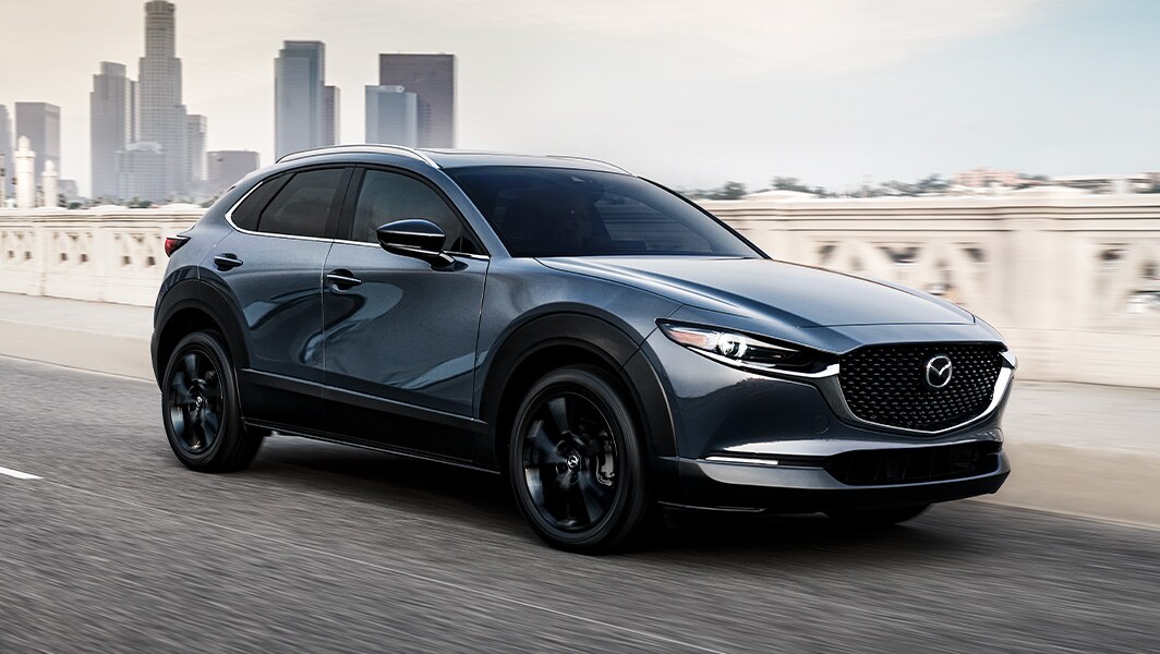The 2022 Mazda CX-5 vs. The 2022 Mazda CX-30 at Jack Giambalvo Mazda | Dark Silver 2022 Mazda CX-30 Driving On Bridge Leaving City