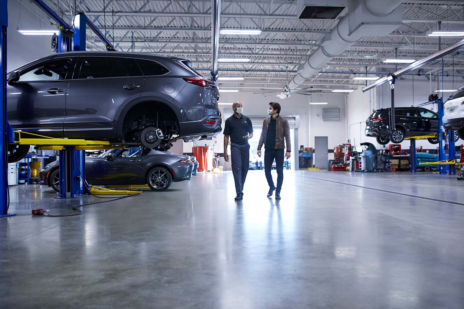 Difference between synthetic oil & conventional oil at Jack Giambalvo Mazda | Mazda service technician talking with customer in service garage