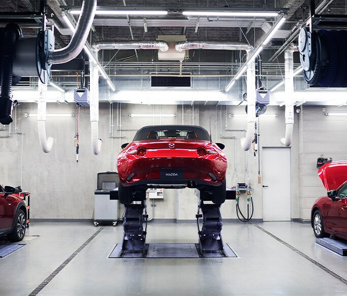 Best MPG At Jack Giambalvo Mazda in York, PA | Red 2022 Mazda MX-5 on car lift while in a garage with a lot of white light