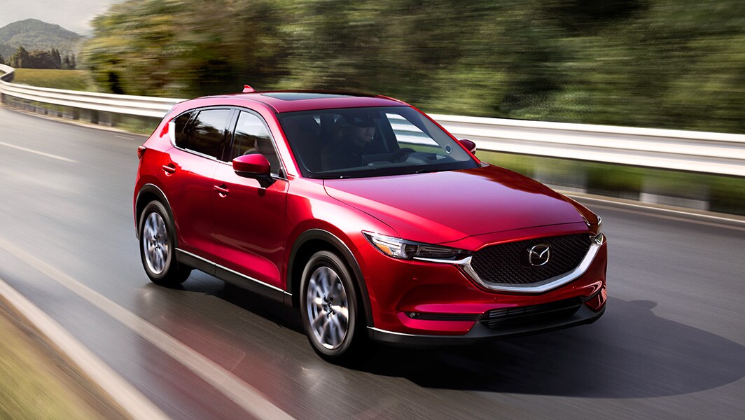 The 2022 Mazda CX-5 vs. The 2022 Mazda CX-30 at Jack Giambalvo Mazda | Red 2022 Mazda CX-5 Driving On Road By Trees