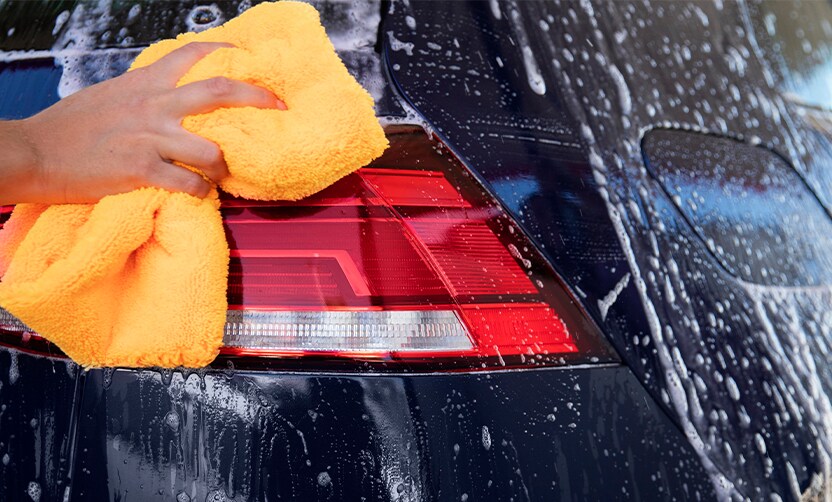 Extend the Life of Your Vehicle at Jack Giambalvo Mazda in York, PA | Person using a bright orange towel rag to clean his navy blue car