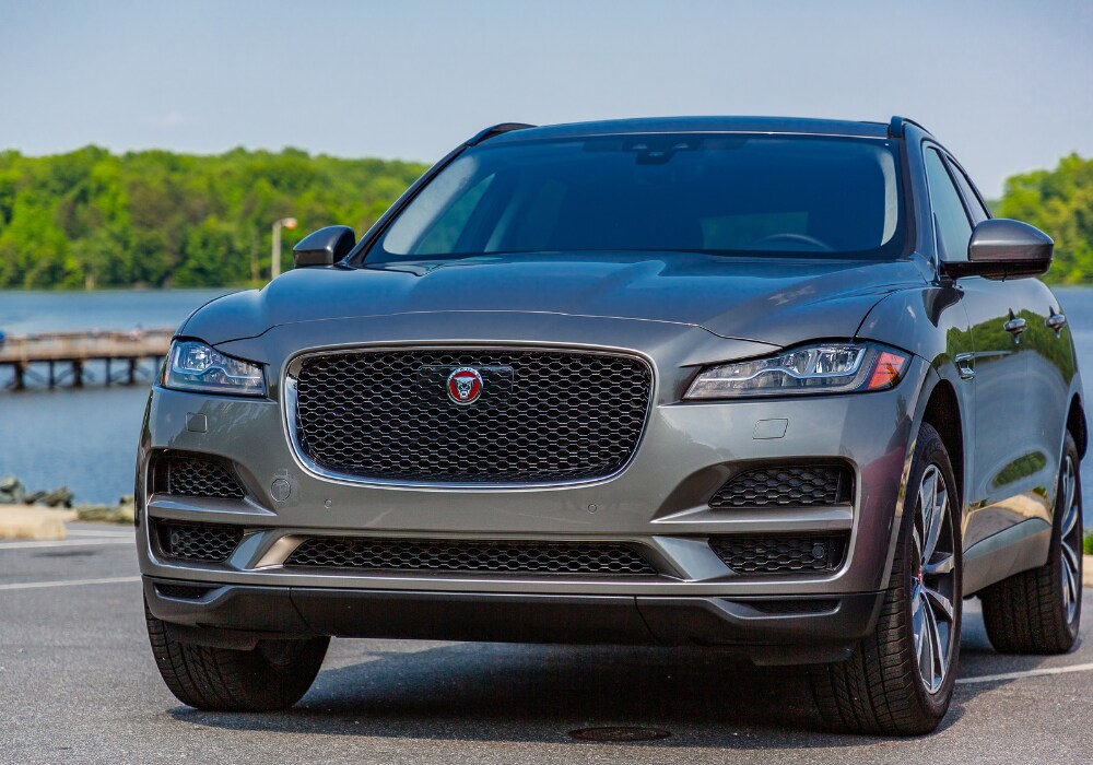 used-jaguar-for-sale.png Silver Jaguar SUV parked in front of a lake with trees in the background