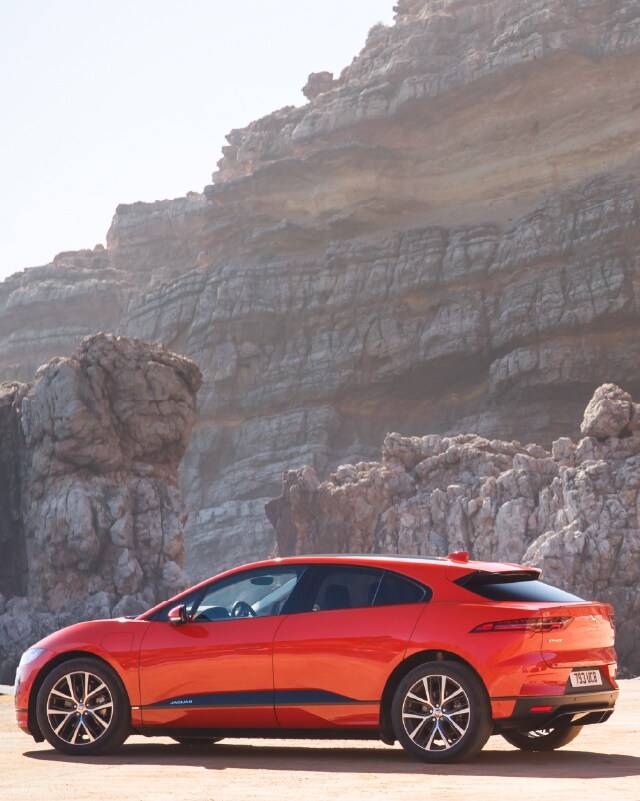 RED JAGUAR I-PACE PARKED ON THE BEACH.