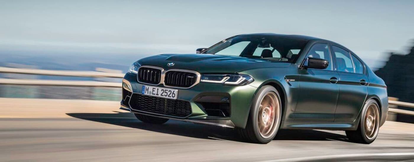 BMW Lease Deals 2021 BMW M5 CS.jpg A green 2021 BMW M5 CS is driving on a highway in front of a guardrail after signing a BMW lease deal.