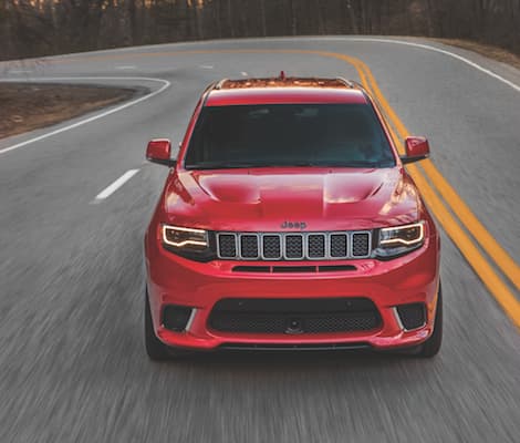 2019 Jeep Grand Cherokee A red 2019 Jeep Grand Cherokee driving down an open road