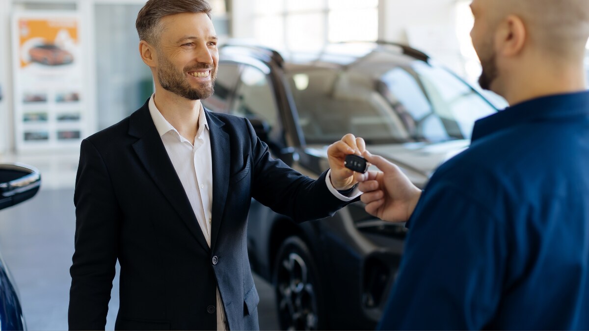 A salesperson handing a key fob over to a man in a dealership A salesperson handing a key fob over to a man in a dealership