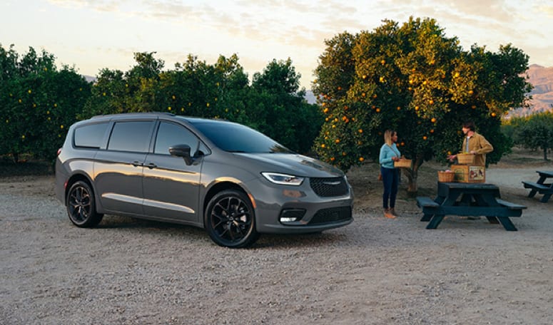 grey Chrysler Pacifica minivan parked at an orange orchard with the driver and passenger by a picnic table