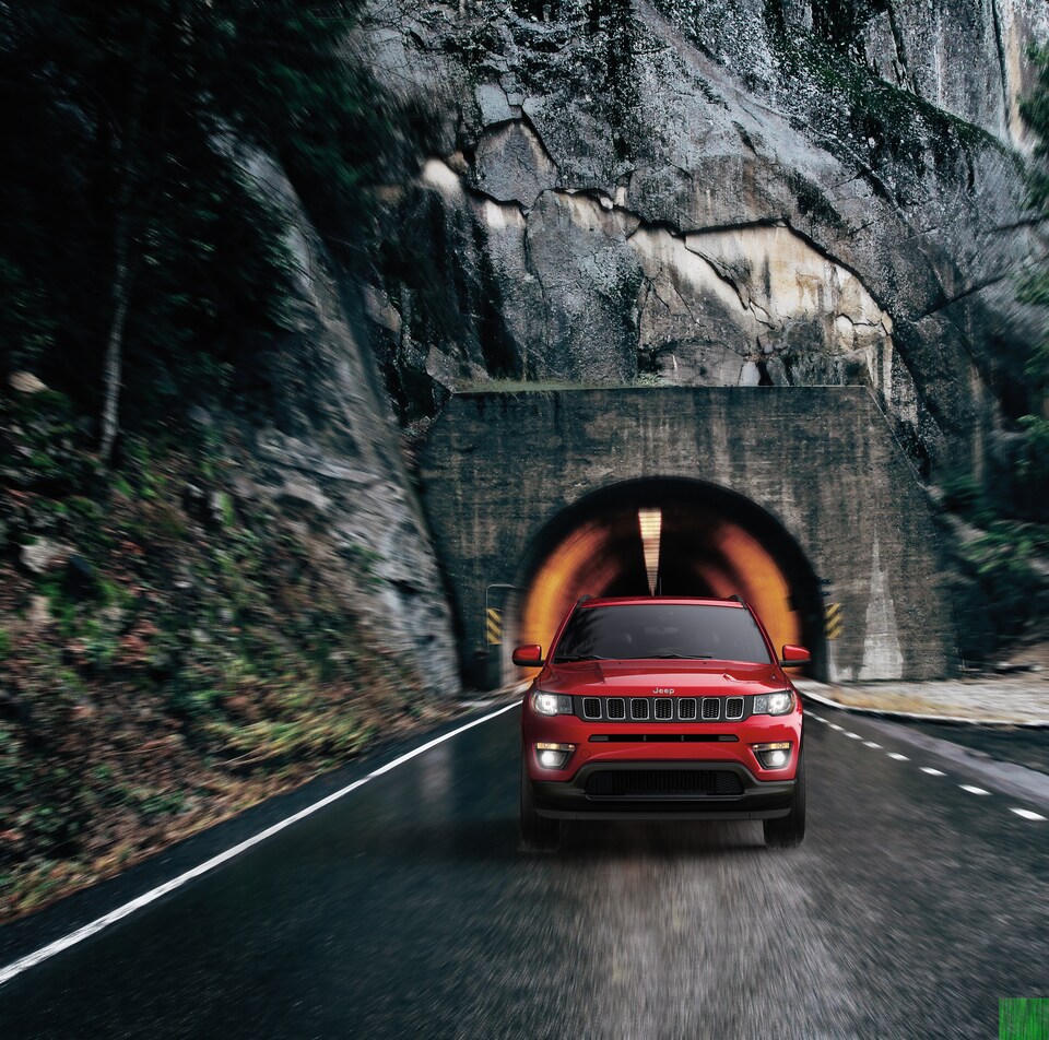 2021-Jeep-Compass-Latitude-SUV-L04.png red Jeep Compass SUV driving out of a mountain tunnel
