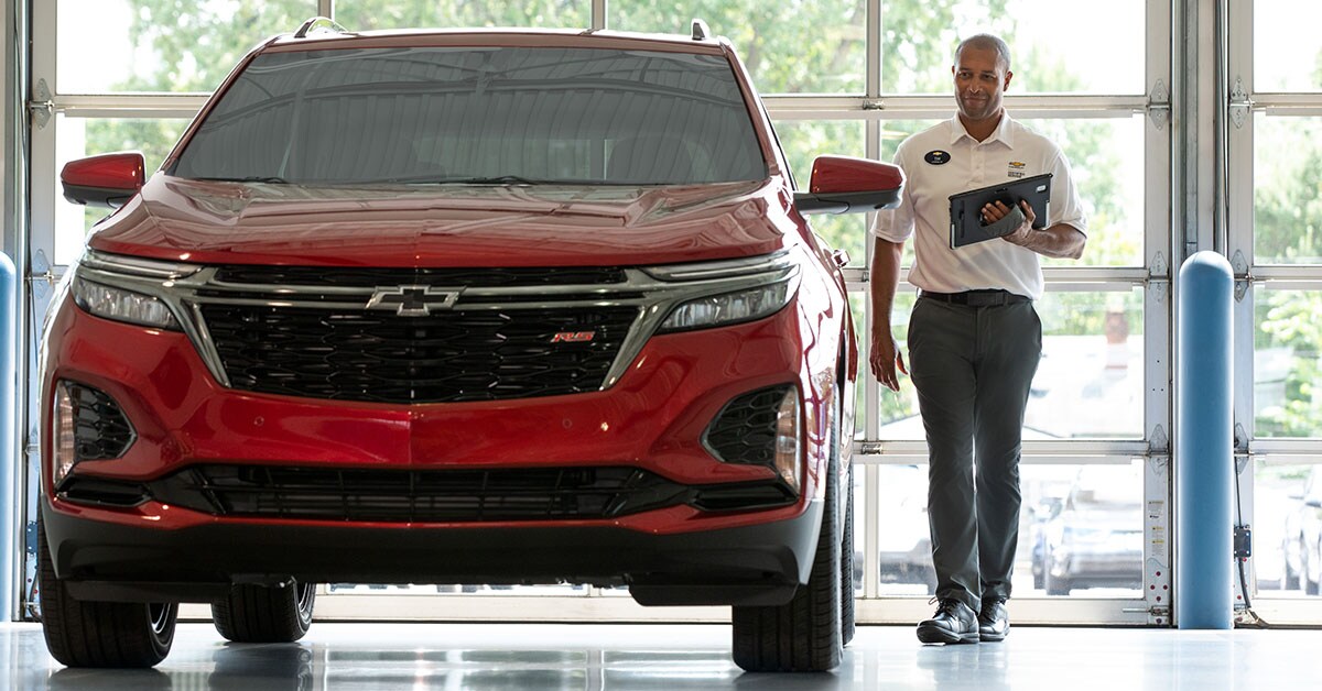 Chevy_Service_ServiceBay_2_1200x628.jpg Chevy service worker examining a vehicle in a service bay