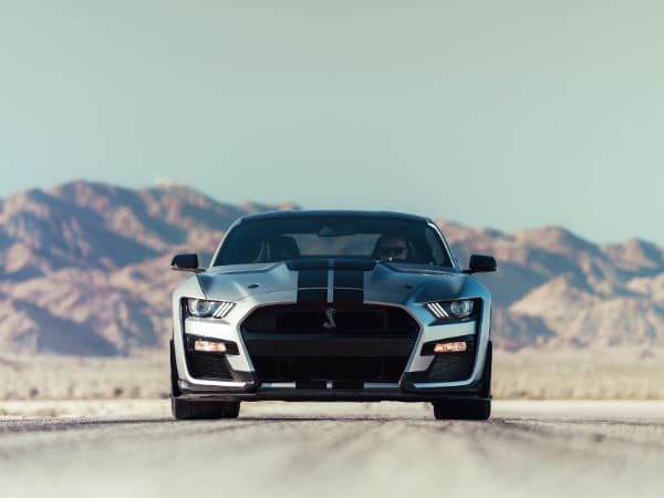 2020 Ford Mustang A silver 2020 Ford Mustang driving down an open road away from the mountains