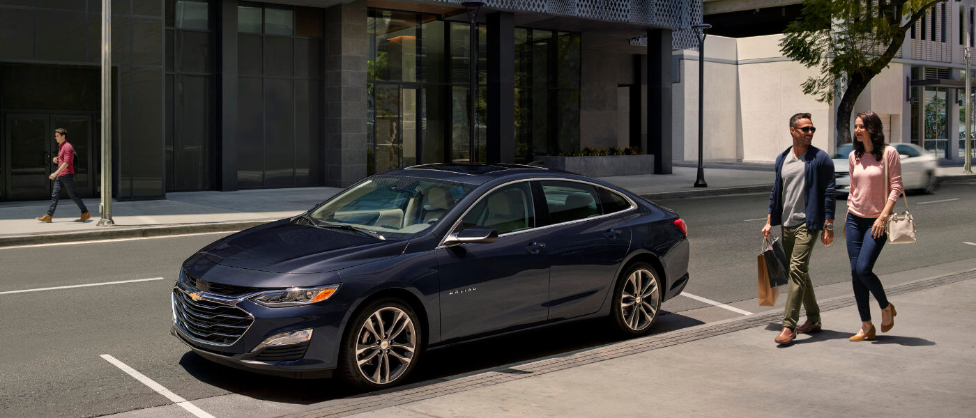 2025 Chevy Malibu parked near sidewalk with couple