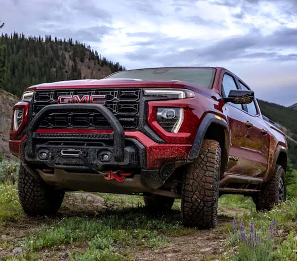 Exterior shot of a 2023 GMC Canyon on a grass field with mountains in the background.