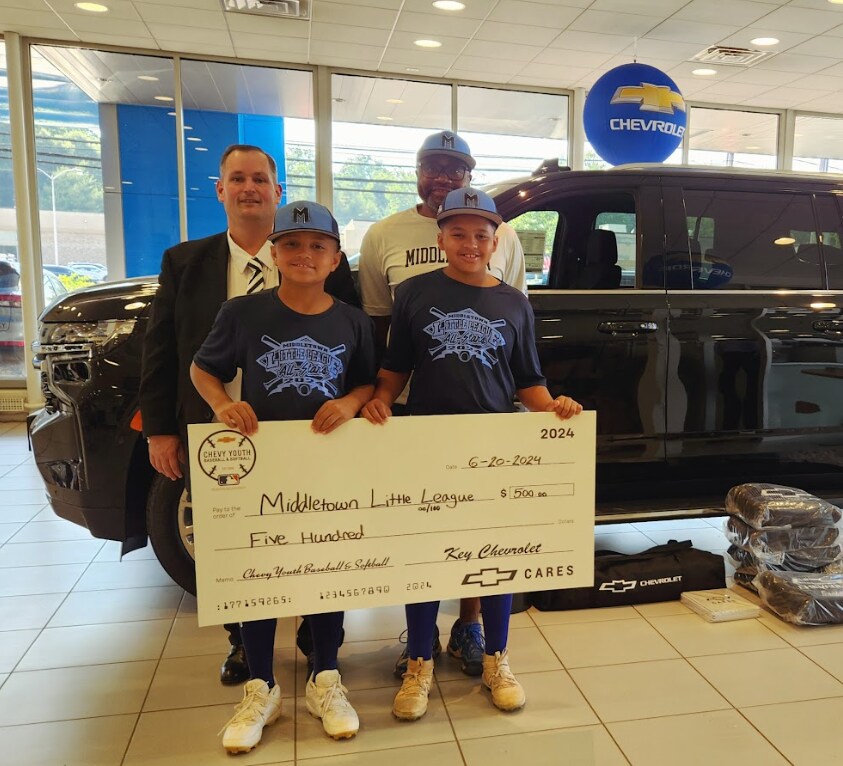 Chevy Dealer in Middletown Two boys wearing baseball caps are holding a novelty check and standing in front of two men and a Chevy SUV in an auto showroom