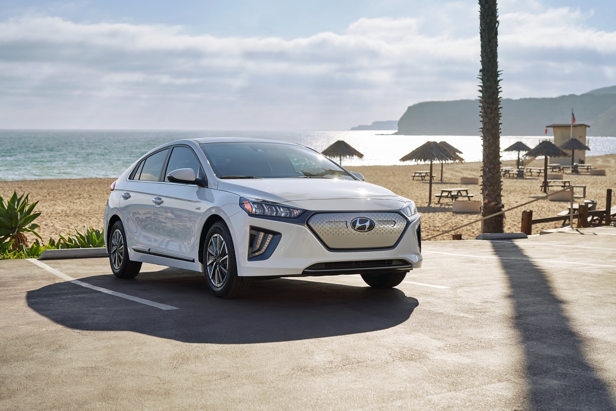 2021-Hyundai-IoniqElectric-Limited-Hatchback-L13.png white Hyundai Ioniq electric car parked next to the beach