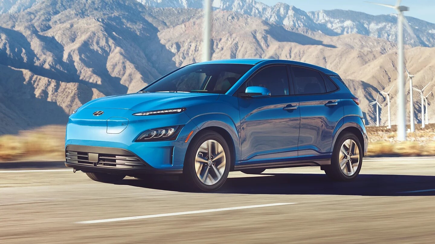 blue Hyundai Kona driving in a desert area next to wind turbines