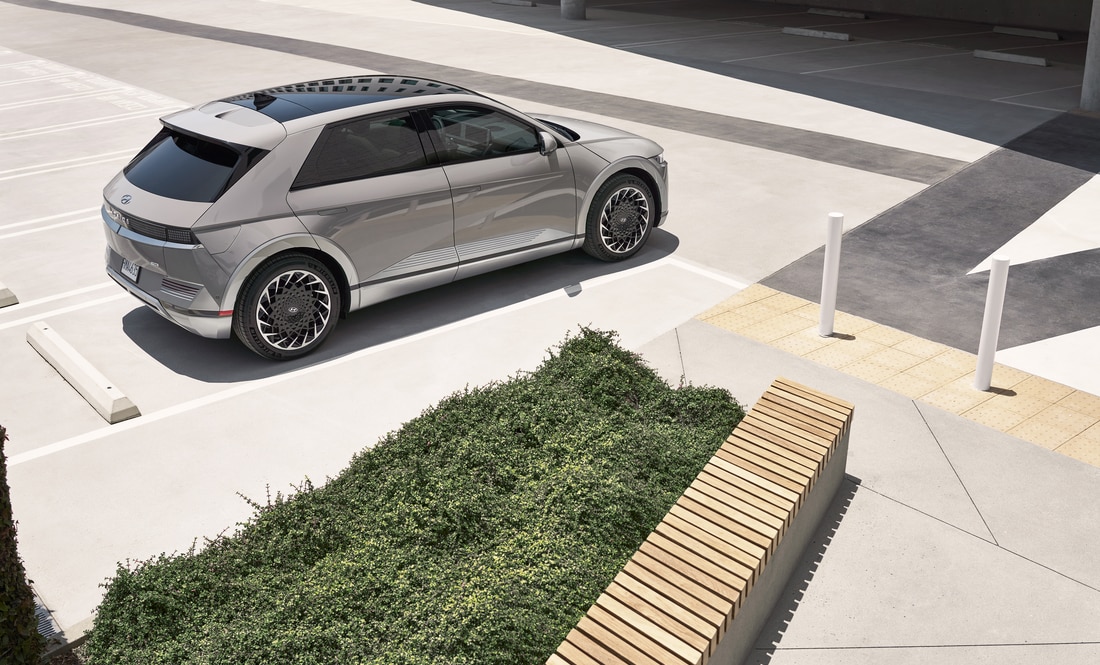 2022-Hyundai-IONIQ5-Limited-SUV-L23.png silver Hyundai Ioniq 5 electric SUV parked next to a parking structure with greenery