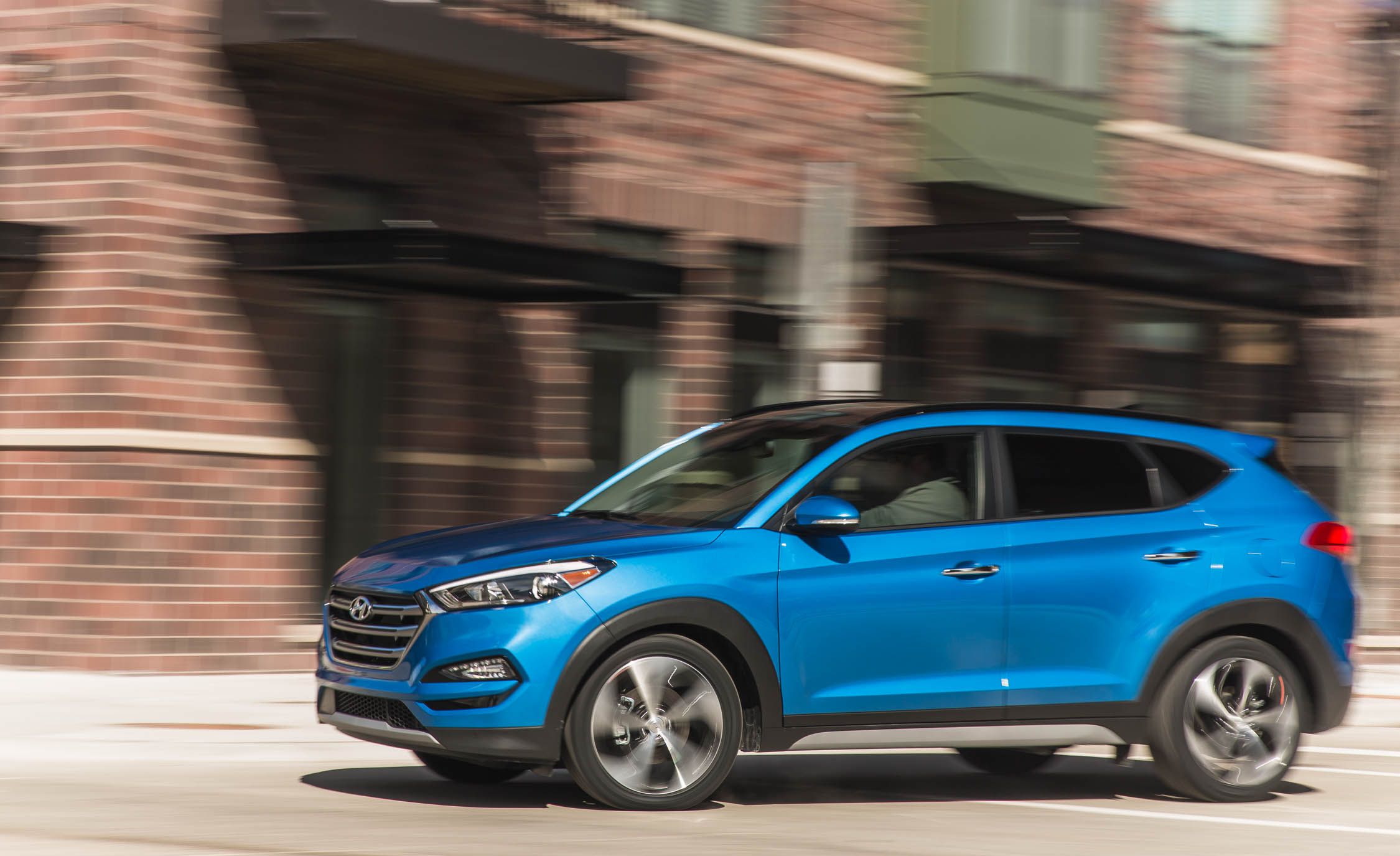 2018 Hyundai Tucson blue Hyundai Tucson SUV driving fast past a brick building