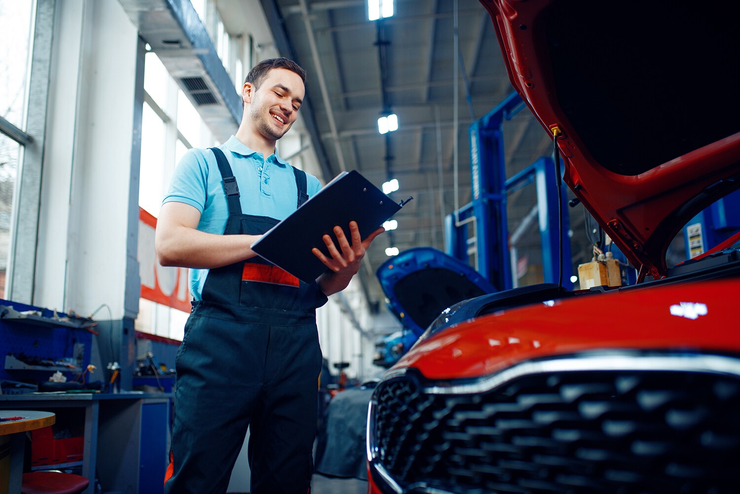 Kia Oil Change Benefits at Kia of New Bern | Service technician writing on clipboard while inspecting Kia vehicle