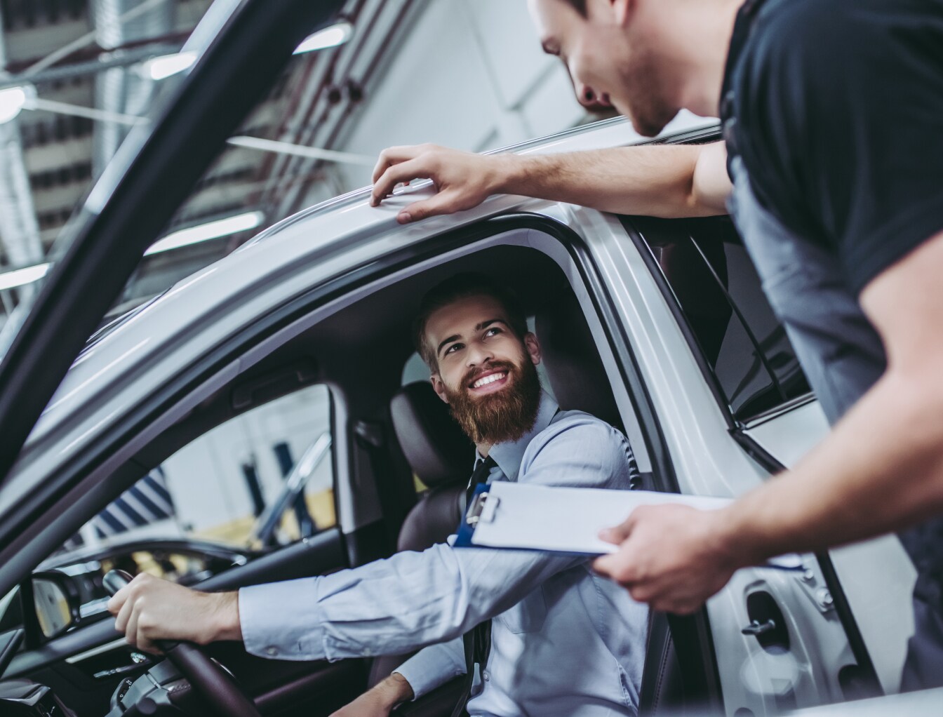 Smiling customer sitting in a car talking with an auto mechanic during a car service appointment