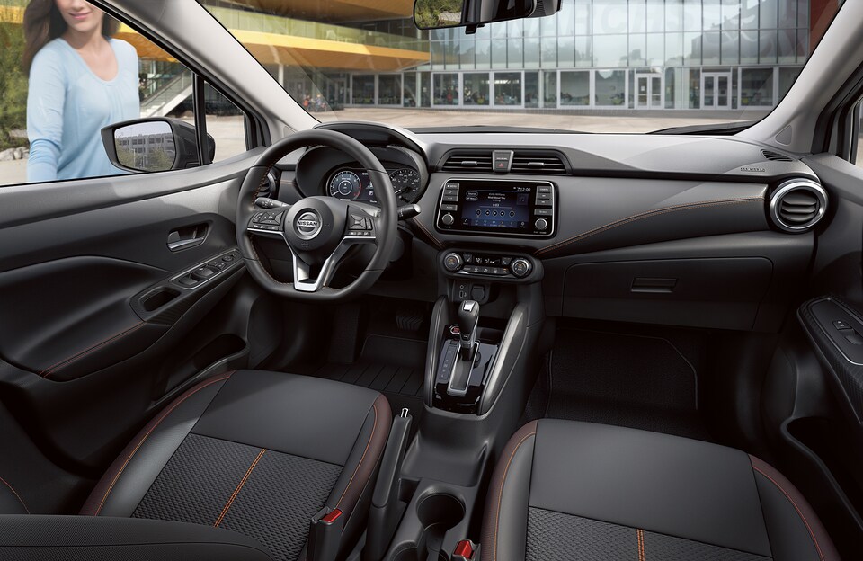 Interior of a Nissan Versa showing the black leather interior and driver's seat features including infotainment system