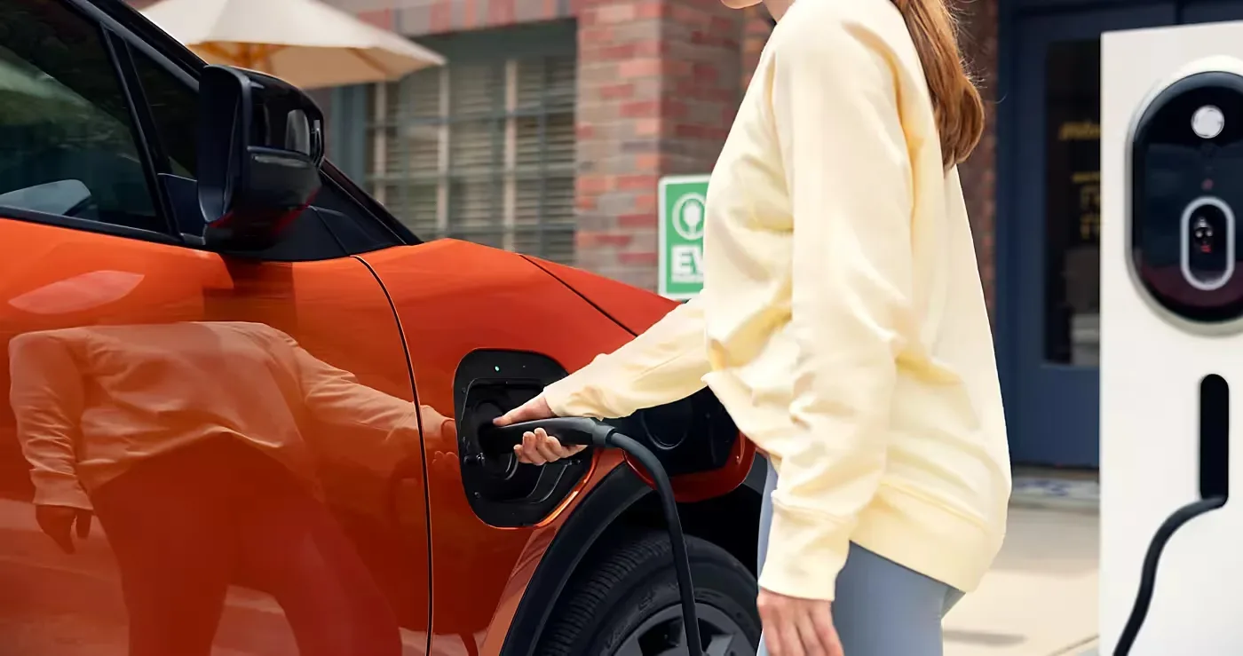 A driver plugging a charging cable into a Subaru electric SUV at a public charging station.