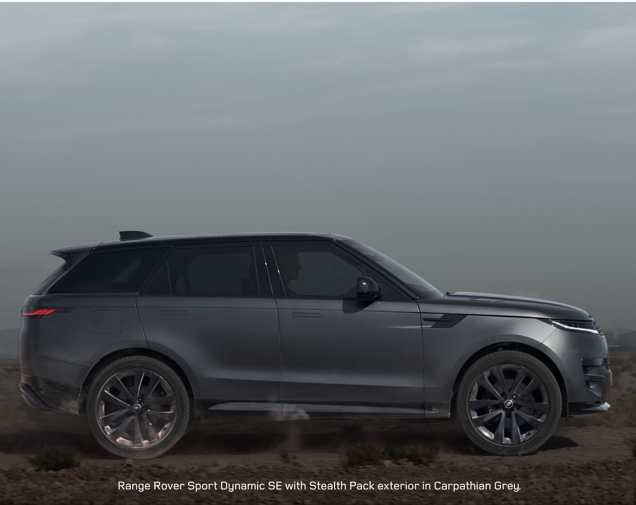 Side profile view of a Range Rover Sport Dynamic SE with Stealth Pack in Carpathian Grey Satin in a rocky desert.